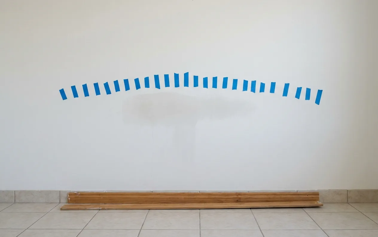 Blue painter's tape marking the edge of a mapped wet area on an interior wall